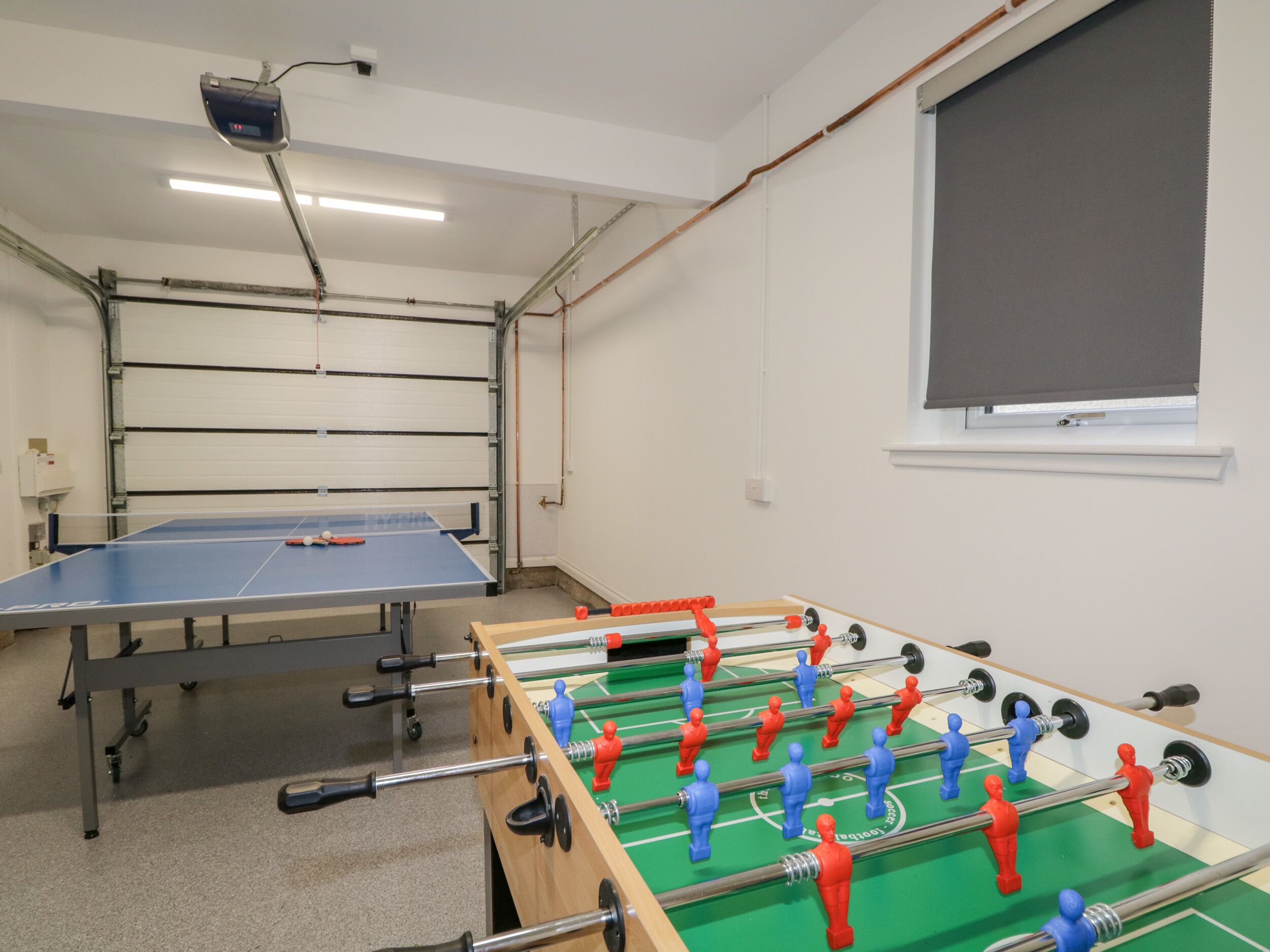 Um quarto com mesa de pingue-pongue, mesa de futebol de mesa e janela com cortina.