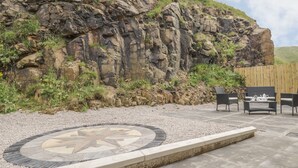 Un patio con una mesa de mosaico de piedra, mobiliario exterior y un acantilado rocoso de fondo.