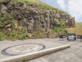 A patio area with a stone mosaic table, outdoor seating, and a rocky cliff backdrop.