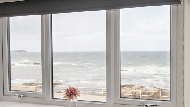 Una ventana con vistas al océano y una flor en un florero.