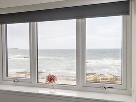 A window with a view of the ocean and a flower in a vase.