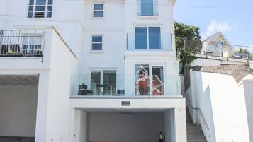 Un edificio de dos plantas con acceso a garaje, un balcón con barandilla de cristal y una escalera que conduce al piso superior.