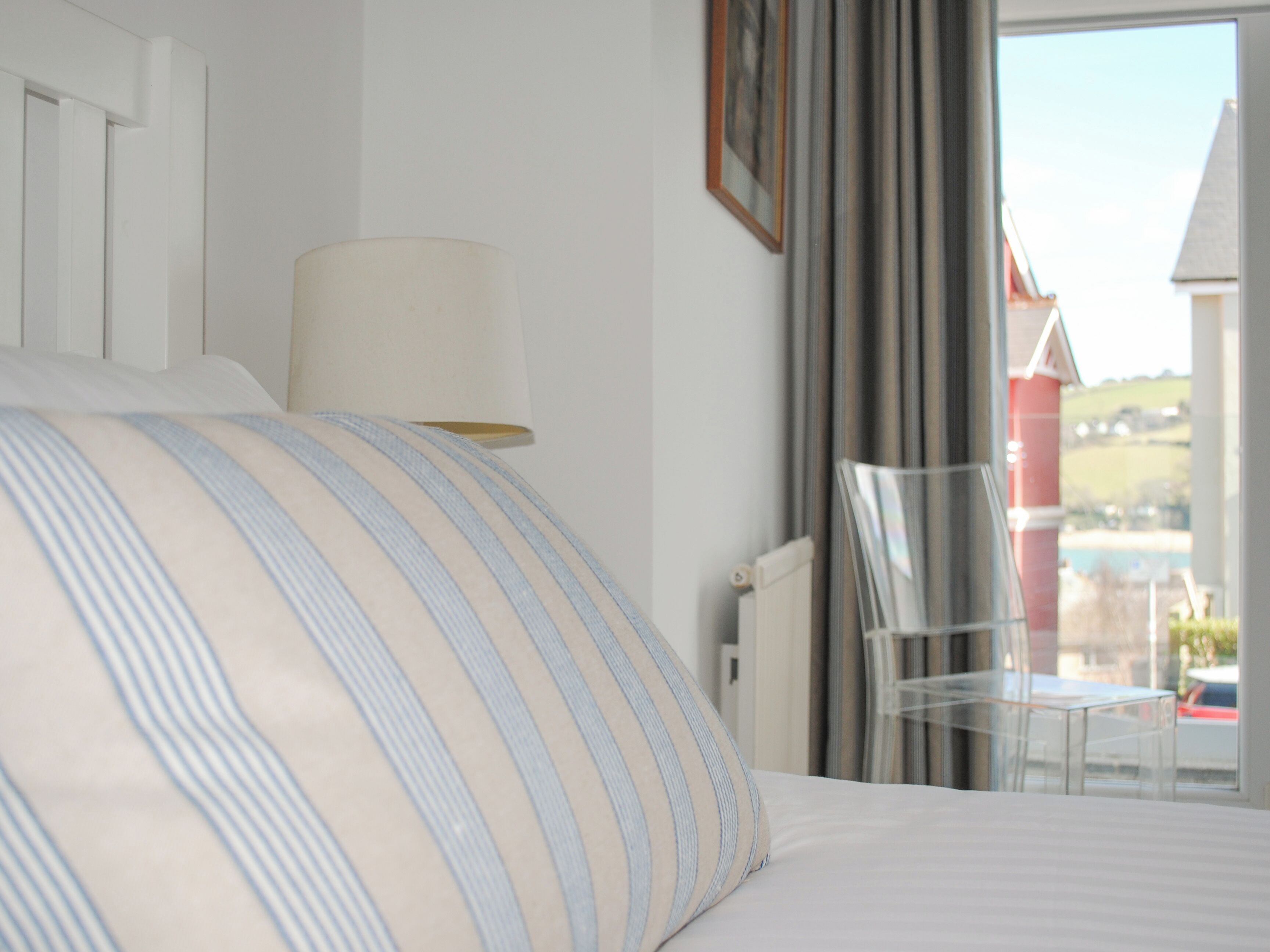 Ein Hotelzimmer mit einem Bett, einer Lampe, einem Sessel und Blick auf ein rotes Gebäude.