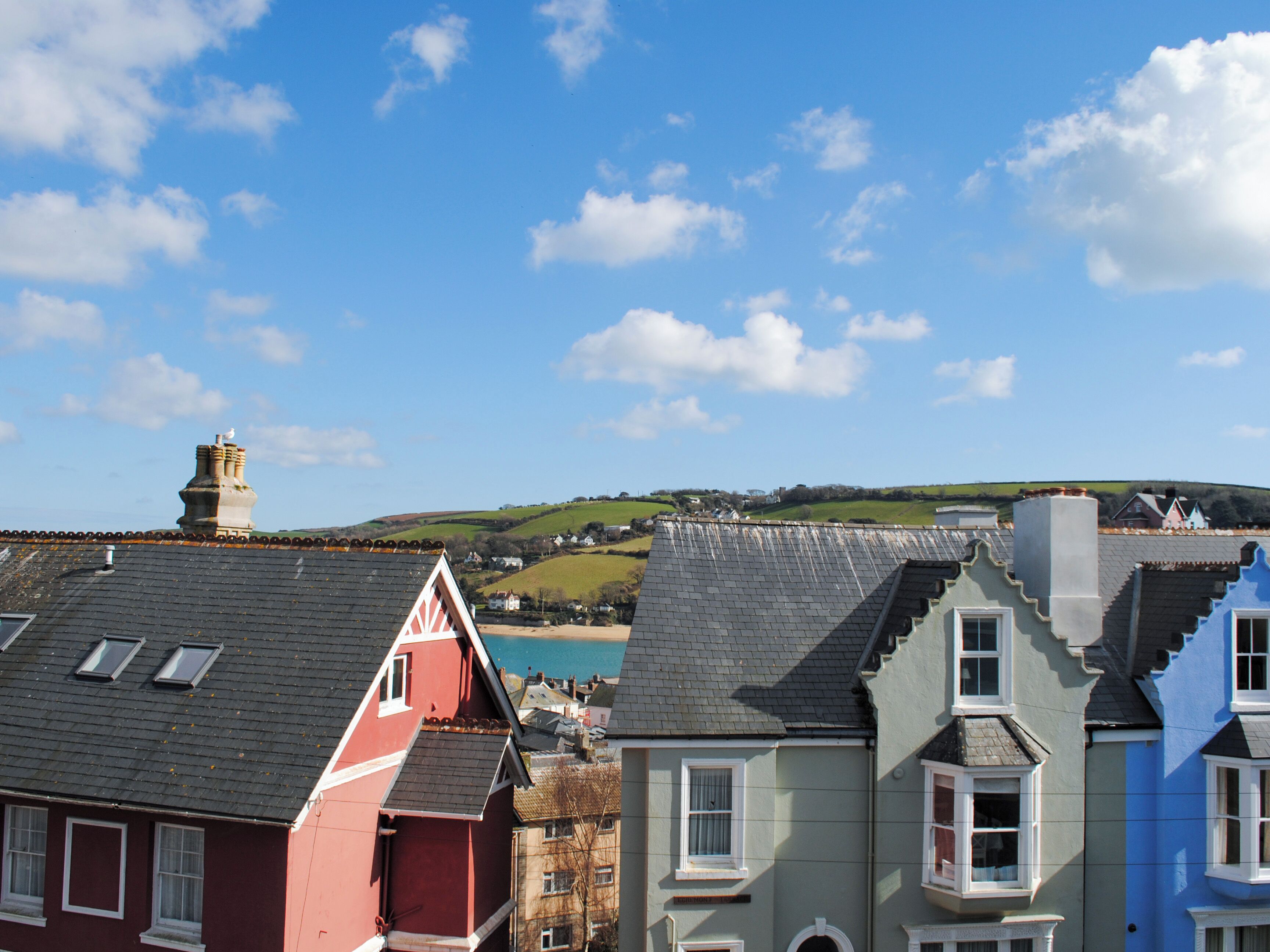 A row of colorful houses with distinct architectural styles, set against a backdrop of a clear blue sky and rolling hills.