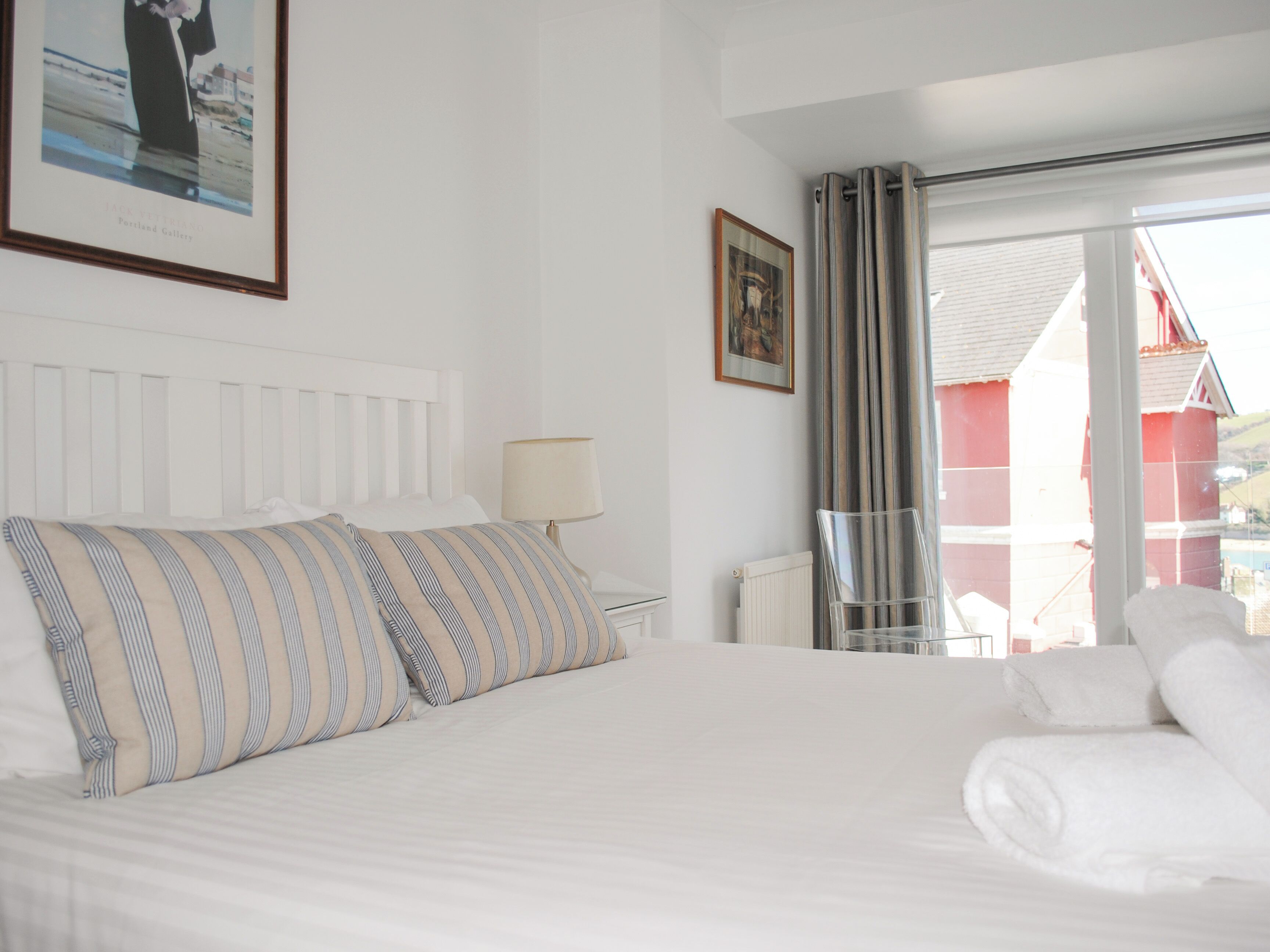 A hotel room with a bed, a nightstand, a lamp, a framed picture, and a view through a window.