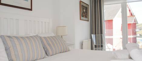 A hotel room with a bed, a nightstand, a lamp, a framed picture, and a view through a window.