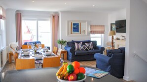 A modern living room with a dining area, featuring a sofa, a coffee table with fruit, and a TV. - Yardarm (Salcombe)
