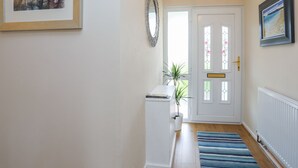 Un couloir avec une porte blanche, un tableau encadré, un miroir et une plante en pot.