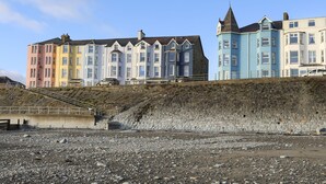 Une rangée de bâtiments colorés donnant sur la mer, avec une plage rocheuse au premier plan.