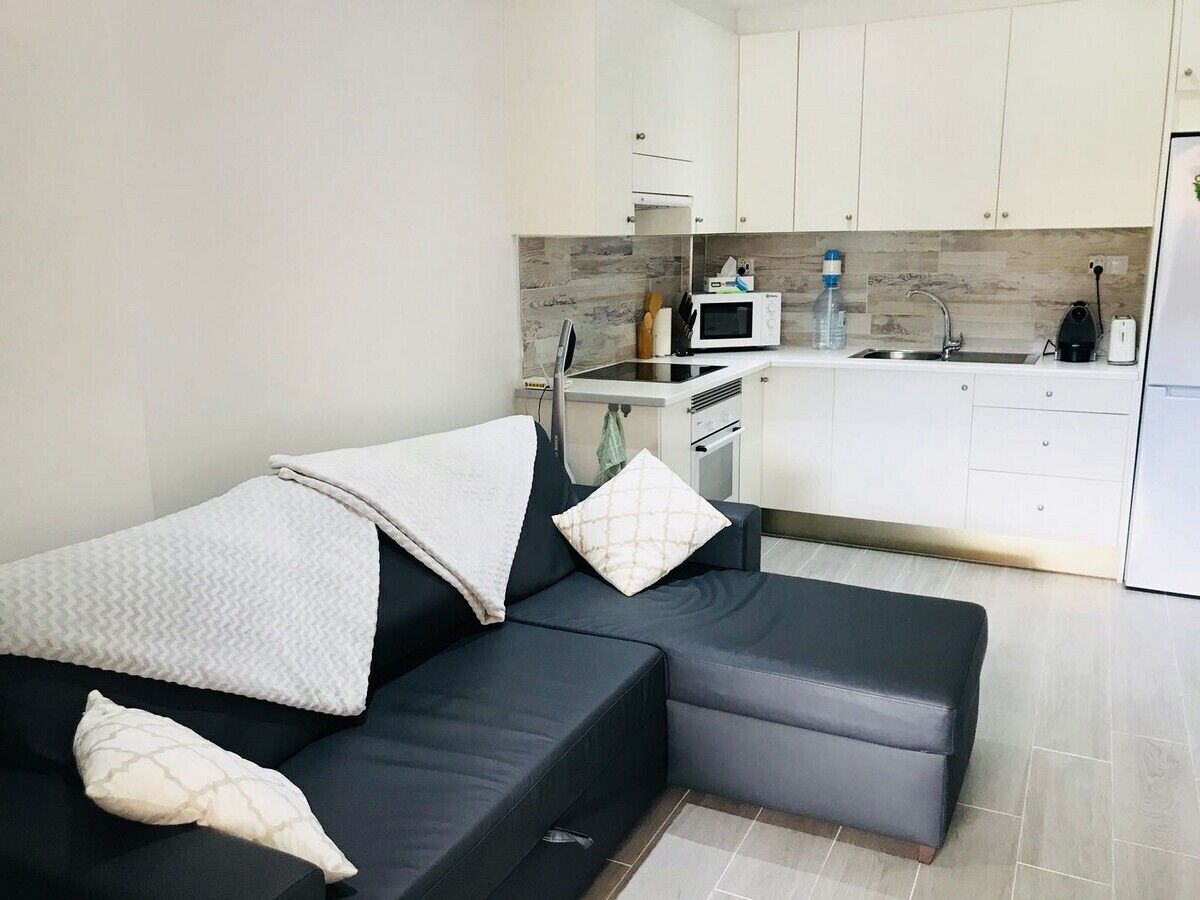 Ein modernes Wohnzimmer mit einem dunkelgrauen Sofa und einer Küchenzeile mit weißen Schränken und einer Mikrowelle.