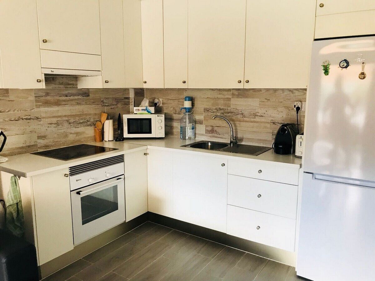 A modern kitchen with white cabinets, a built-in microwave, a sink, and a stainless steel refrigerator.