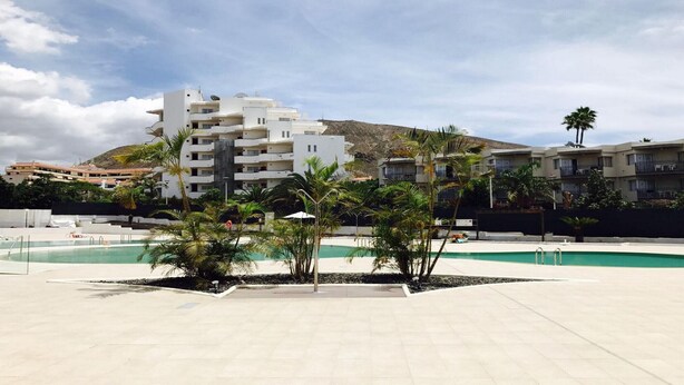 A modern building with multiple balconies, a swimming pool, and palm trees. - San Marino 2 (Los Cristianos)
