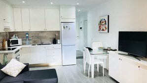 A modern kitchen with white cabinets, a refrigerator, a microwave, and a dining area with a glass table and chairs. - San Marino 2 (Los Cristianos)