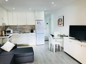 A modern kitchen with white cabinets, a refrigerator, a microwave, and a dining area with a glass table and chairs.