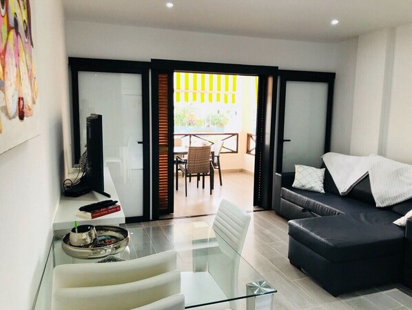 A modern living room with a glass coffee table, a black sofa, and a dining area with a table and chairs.