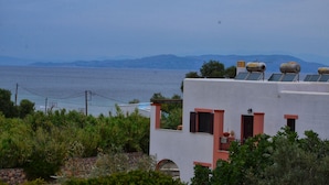 A coastal building with solar panels on the roof, a view of the sea, and mountains in the distance. - Vagia Beach Apartments (Aegina)