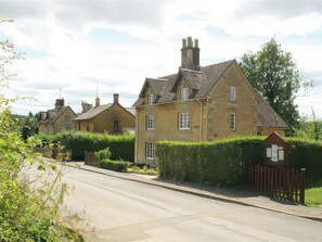 A row of traditional stone houses with pitched roofs, a clear road, and a small wooden gate. - Elm View (Chipping Campden)