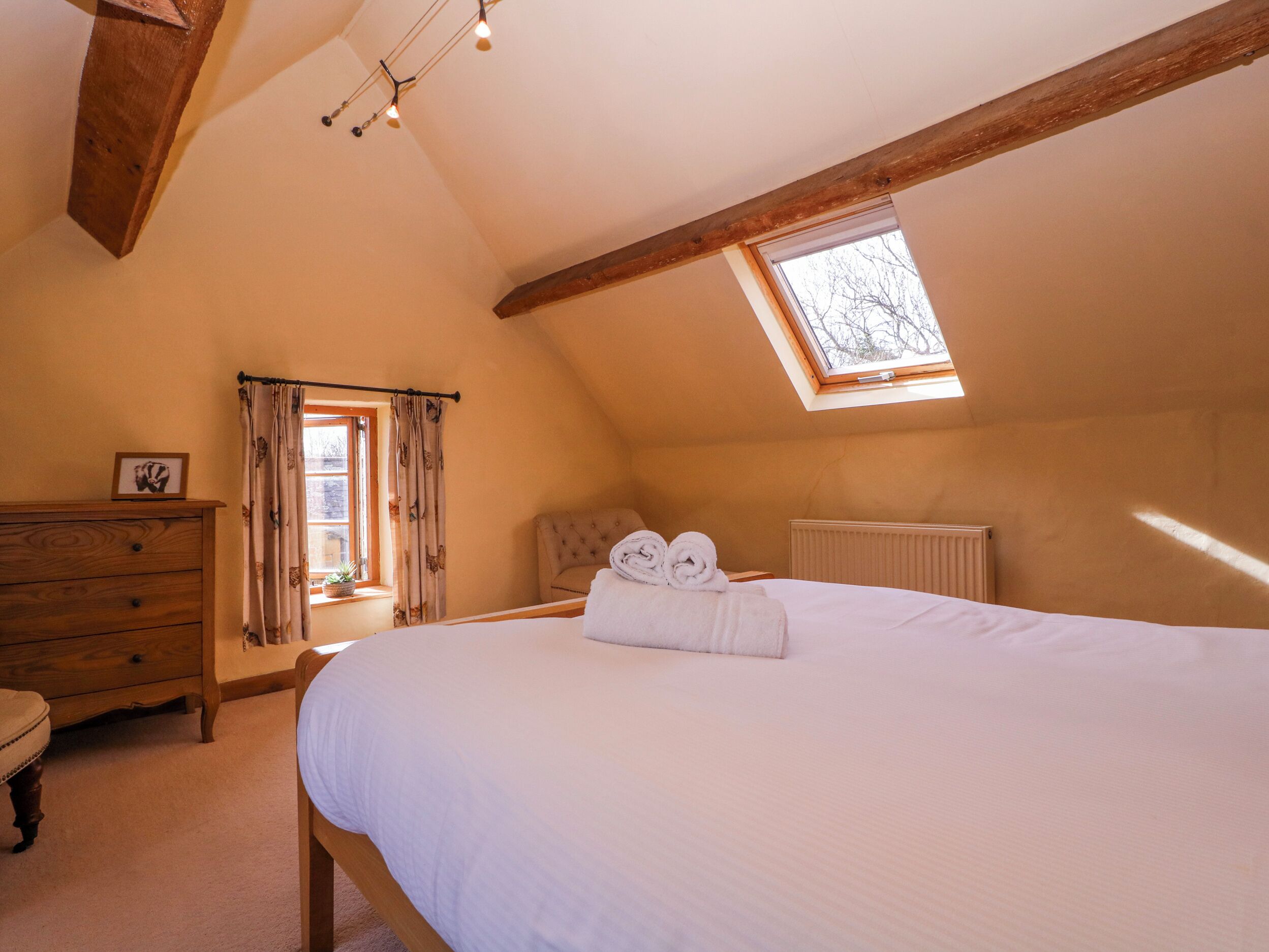 Un dormitorio con una cama grande, vigas de madera, una ventana, un aparador y un radiador.