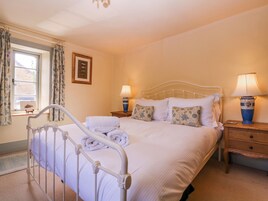A neatly made bed with white linens, two bedside lamps, a wooden nightstand, a framed picture on the wall, and a window with curtains.