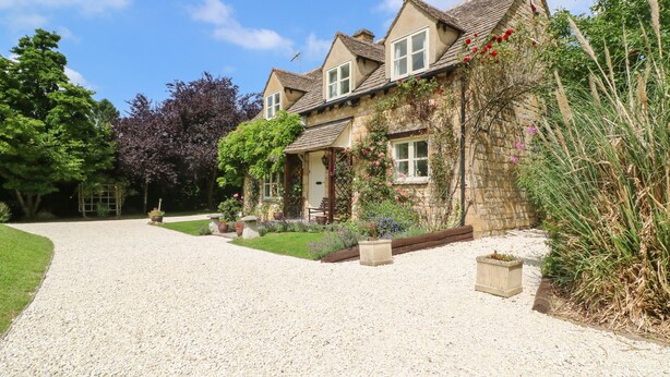 A two-story stone house with a gravel driveway and a well-maintained garden. - Orchard Cottage (Broadway)