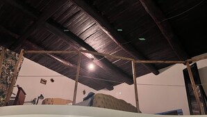 A room with a high ceiling, wooden beams, a bed, a desk, and a chair.