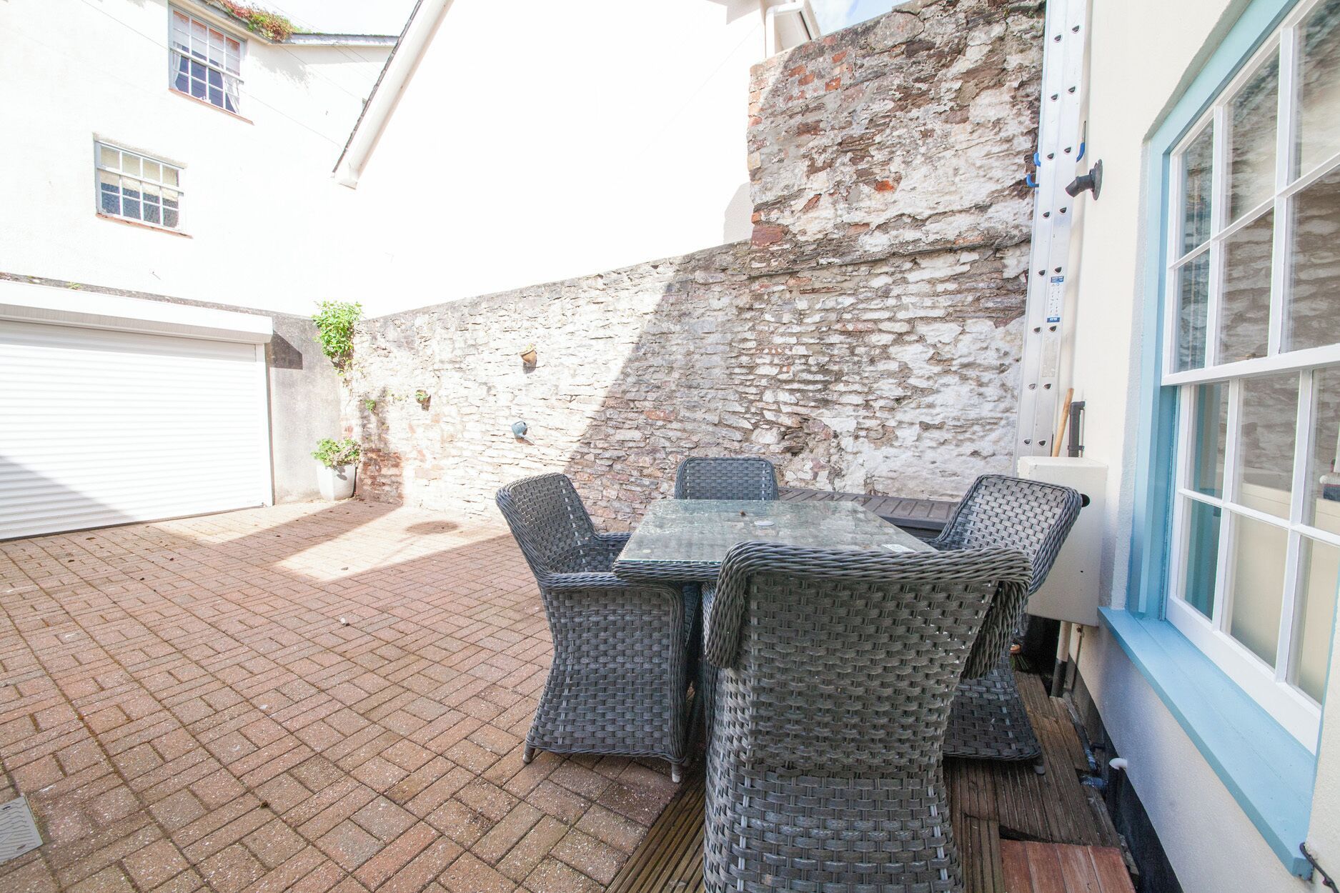 Un patio con una mesa, sillas, un muro de piedra y una ventana.