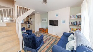Uma sala de estar com sofá, televisão, estante e escada que dá para uma cozinha.