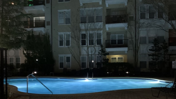 A swimming pool with a paved walkway, surrounded by multi-story buildings with balconies. - Luxurious Condominium (Dunwoody)