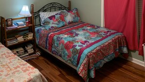 A bedroom with a bed, a nightstand with a lamp, a ceiling fan, and a window with a red curtain. - Luxurious Condominium (Dunwoody)