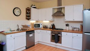A kitchen with white cabinets, a microwave, a stove, a dishwasher, and a clock on the wall. - Aeolus House (Dartmouth)