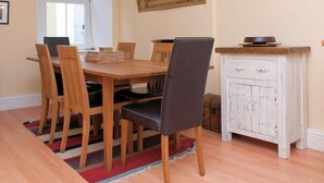 A dining area with a wooden table, four chairs, a white cabinet with drawers, a map on the wall, and a window with blinds. - Aeolus House (Dartmouth)