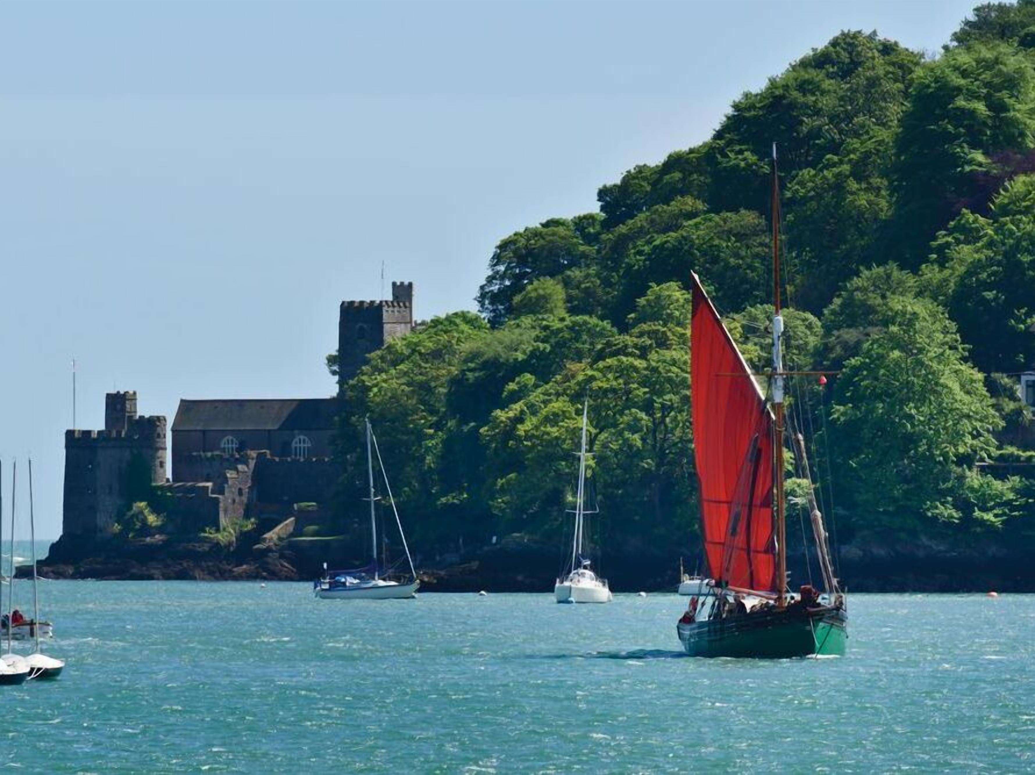 A coastal scene with a sailboat in the foreground and a castle-like structure in the background.