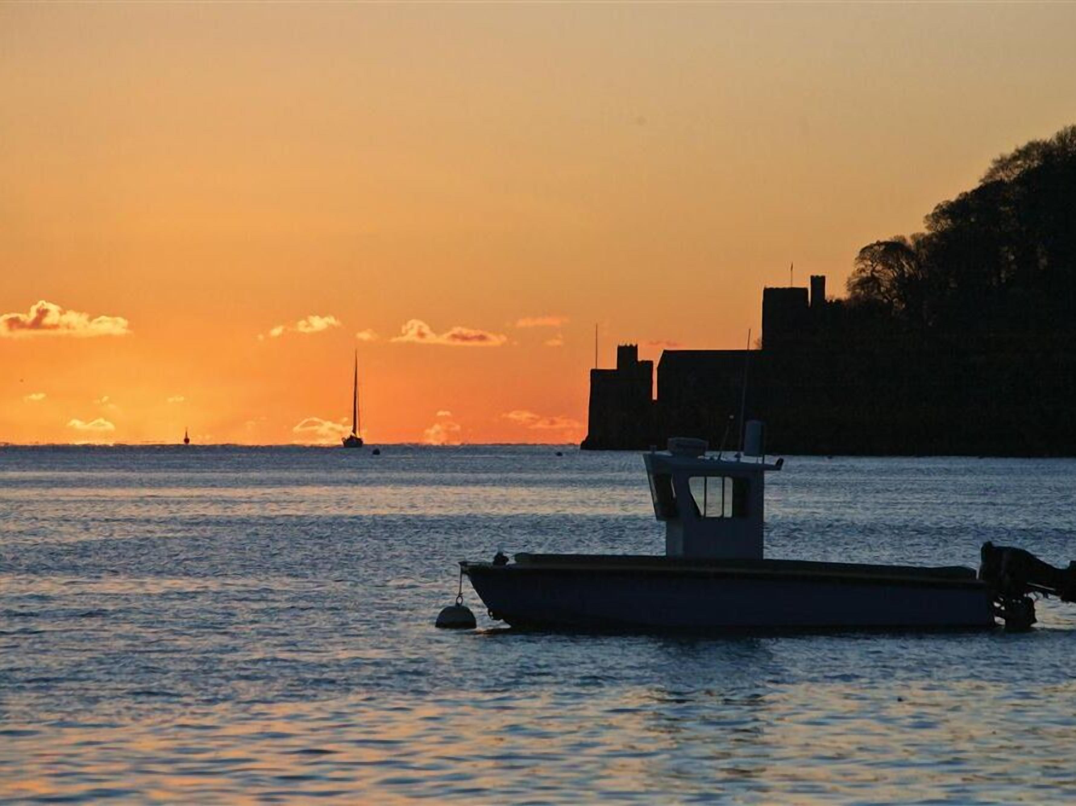 A boat anchored near a shoreline with a sunset in the background.