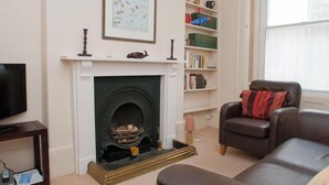 A living room with a fireplace, a bookshelf, a leather sofa, and a television. - Aeolus House (Dartmouth)