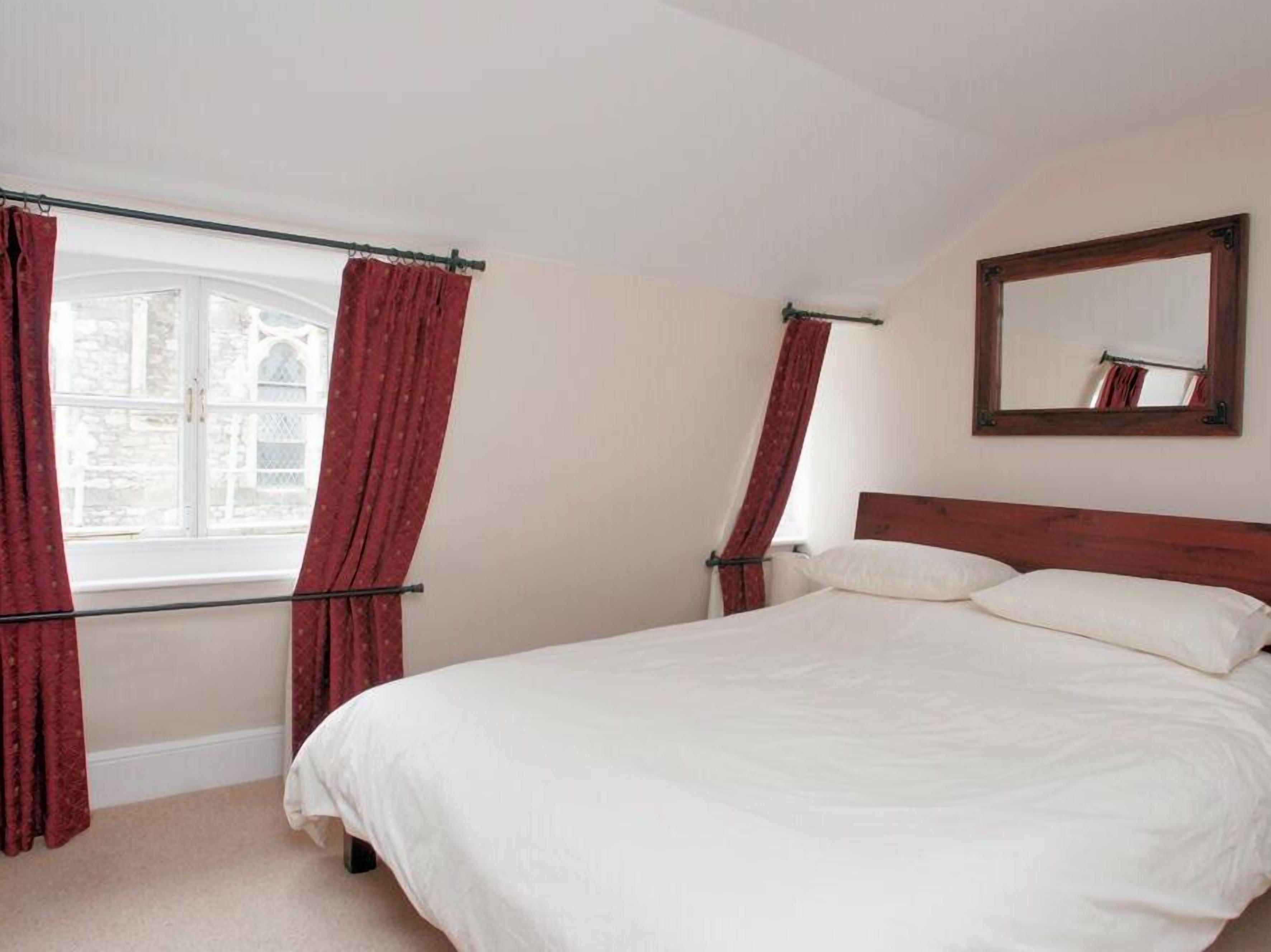 A bedroom with a large bed, a window with red curtains, and a mirror on the wall.