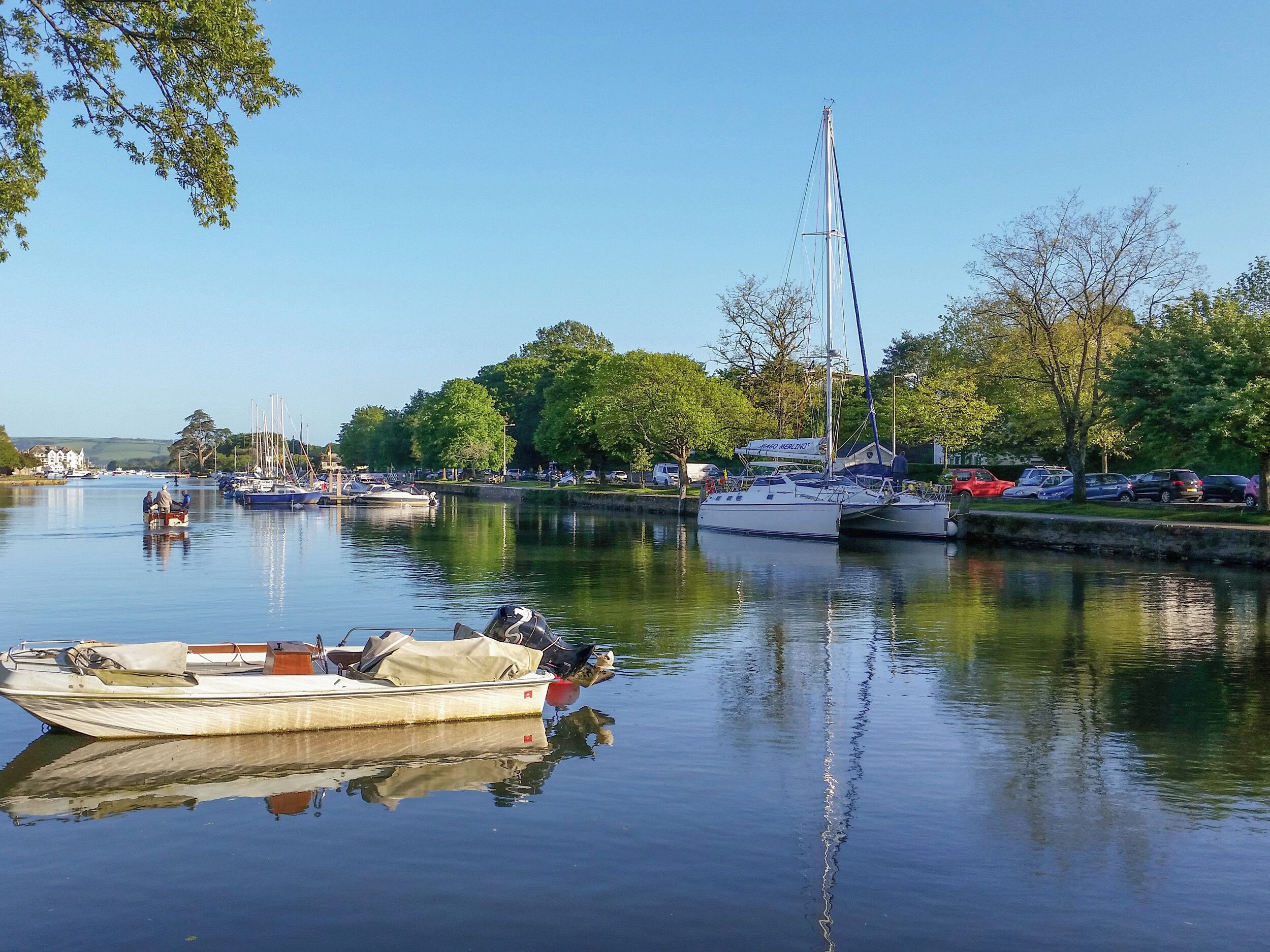 Een rustige haven met verschillende boten afgemeerd, een heldere lucht en bomen langs de oever.