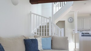 Una sala de estar con un sofá seccional color beige, una escalera y una zona de cocina.