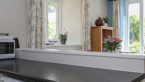 Una cocina con microondas, una ventana con cortinas y una repisa con un jarrón de flores.