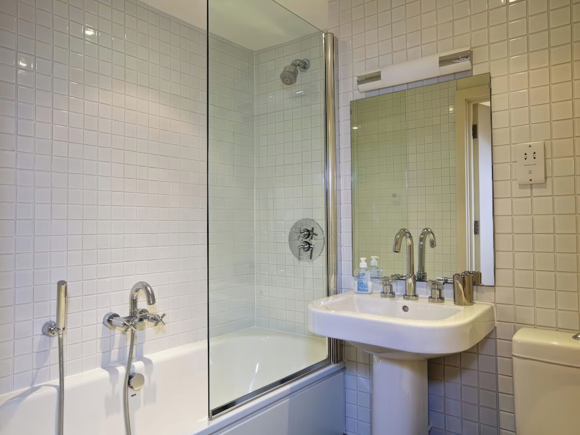 A modern bathroom with a glass-enclosed shower, a white bathtub, and a sink with a mirror above it.