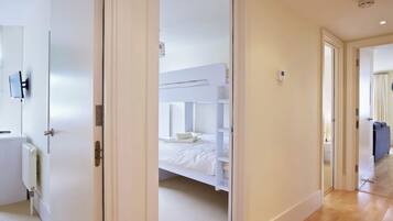 Une chambre d’hôtel moderne équipée d’un lit superposé, d’un téléviseur à écran plat fixé au mur et d’une salle de bain visible avec des toilettes et un lavabo.