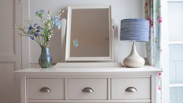 A white dresser with a mirror, a vase with flowers, and a lamp.