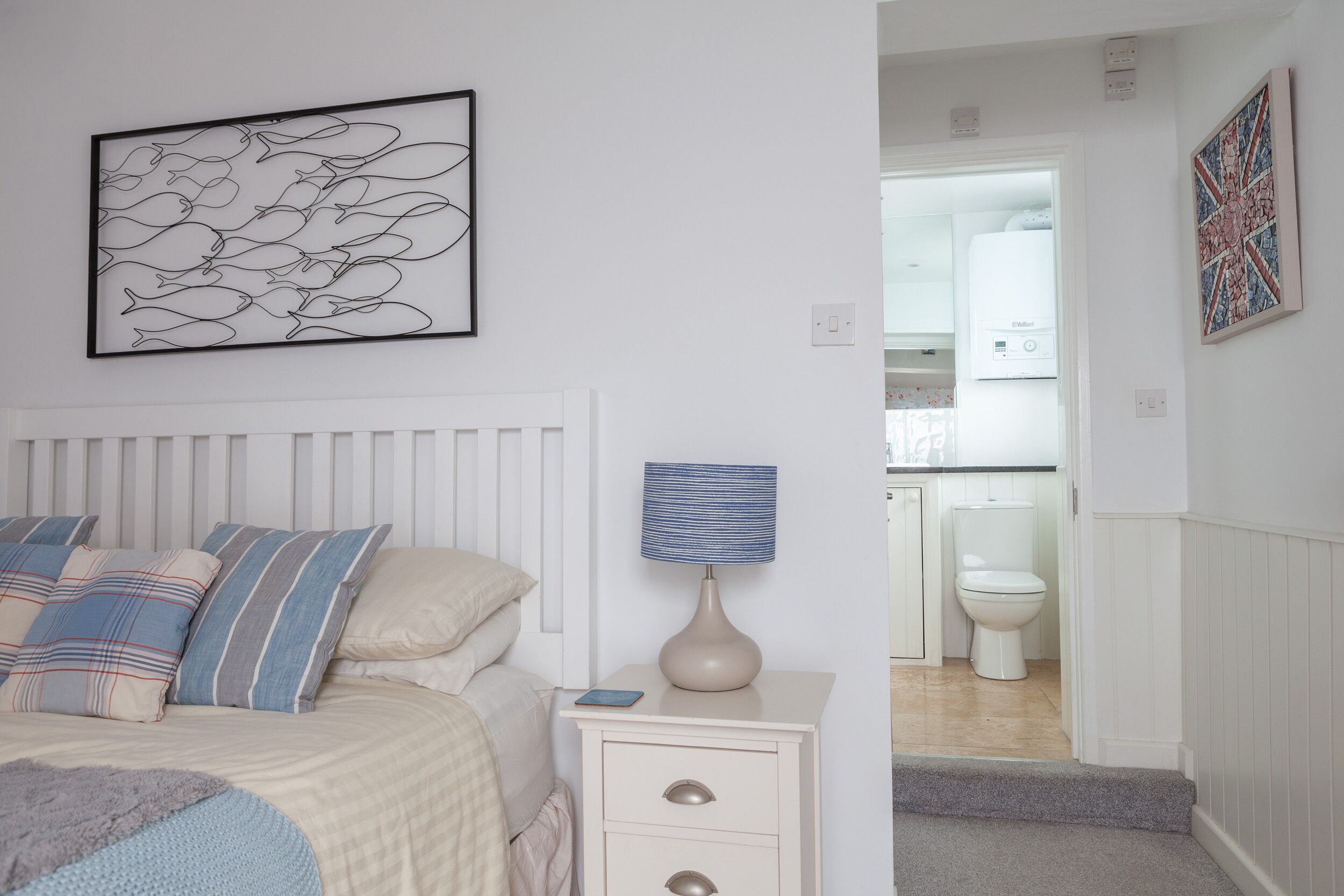 Un dormitorio con cama, mesita de noche, lámpara y una obra de arte en la pared.
