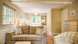 Un salon chaleureux avec un canapé beige, un fauteuil à carreaux et un plancher en bois.