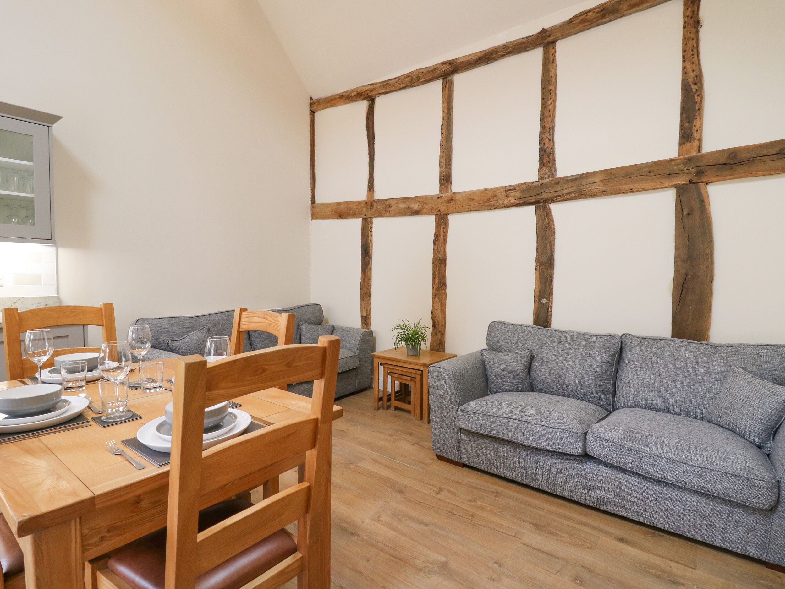 Un comedor con una mesa de madera dispuesta para cuatro personas, un sofá gris y un banco de madera.