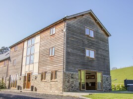 Un edificio de dos pisos con cimientos de piedra y revestimiento de madera, con varias ventanas y una entrada amplia y abierta.