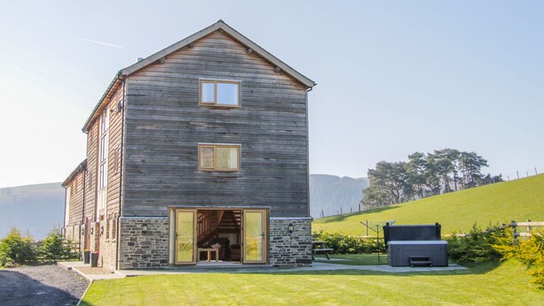 Un bâtiment en bois à deux étages, doté de fondations en pierre, d’un escalier menant à l’étage supérieur et d’un petit espace extérieur aménagé pour s’asseoir.