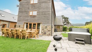 Une maison en bois à deux étages, dotée d’un patio comprenant un barbecue et des meubles d’extérieur.