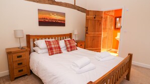 Une chambre à coucher avec un lit en bois, du linge de lit blanc, une table de chevet avec une lampe, une armoire en bois et un tableau représentant un coucher de soleil.