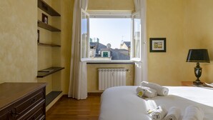 Une chambre d’hôtel avec un lit, une commode, une fenêtre avec des rideaux, un radiateur et une lampe.