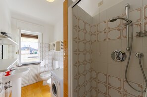 Une petite salle de bain équipée d’un lave-linge, de toilettes et d’une douche.